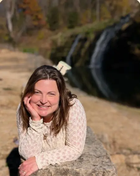 Polly Fleming smiling, resting on a stone ledge beside a waterfall
